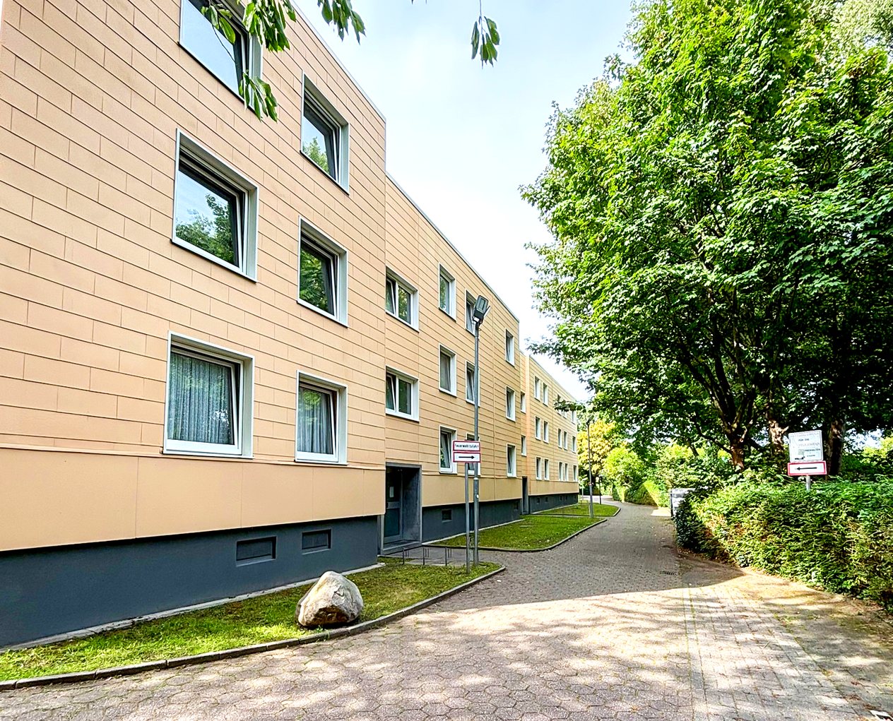 Mehrfamilienhaus in Düsseldorf mit heller Fassade, Bäumen und gepflastertem Weg